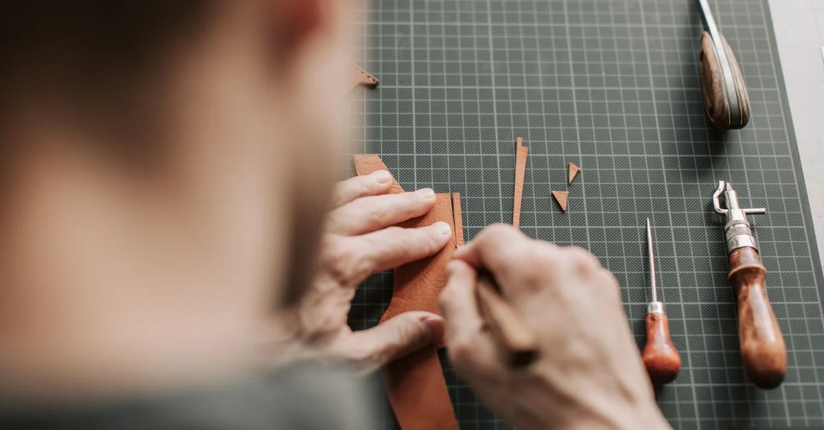 Gros plan sur un artisan coupant du cuir avec des outils dans un atelier.