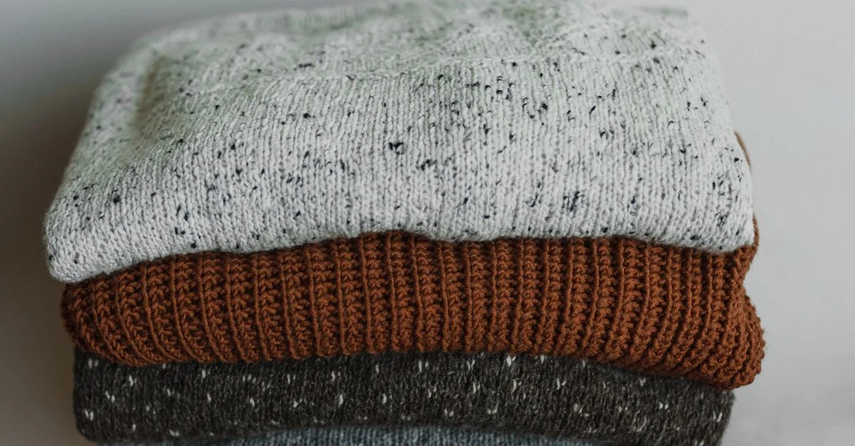 Gros plan de pulls en tricot pliés dans des tons neutres, parfaits pour la mode automnale et hivernale.