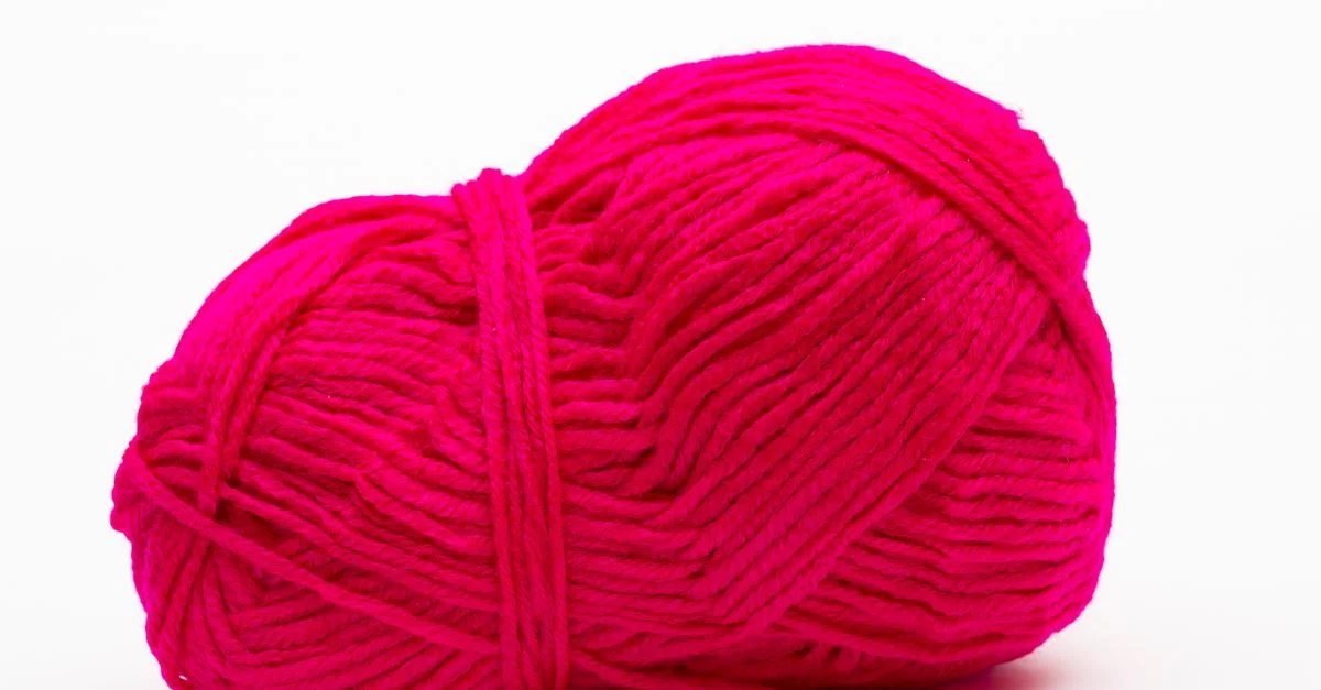 Pelote de laine rose vif sur fond blanc, idéale pour les projets de tricot.