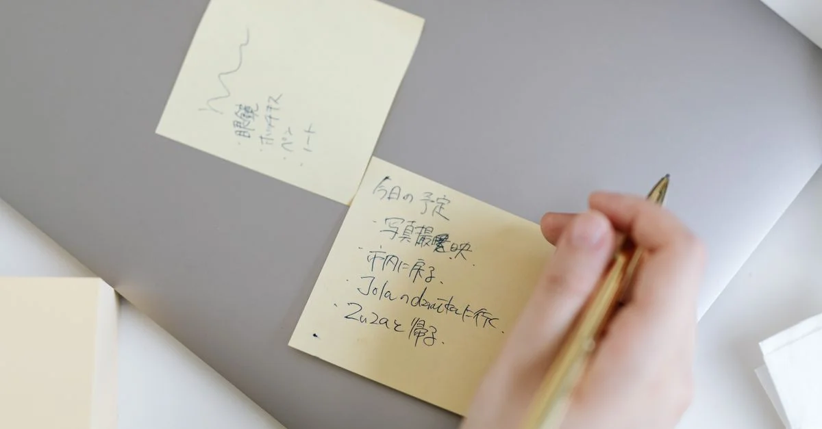 Gros plan sur une main écrivant des notes sur des post-it placés sur un ordinateur portable, mettant en avant la planification et l'organisation.